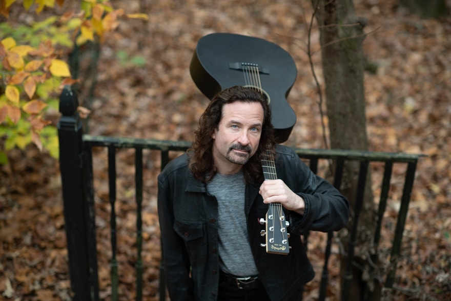 Doug Hartley holding an acoustic guitar outdoors